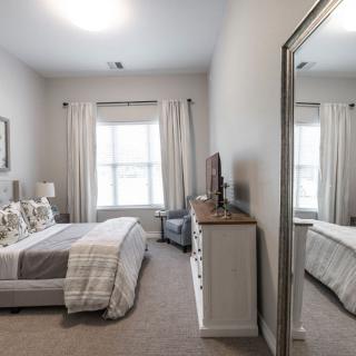 A modern bedroom with a large mirror, neatly arranged furniture, and neutral decor.