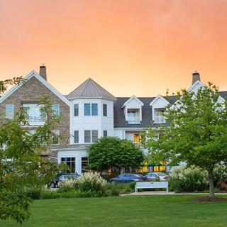 A charming residential building set against a vibrant sunset, surrounded by lush greenery and well-maintained lawns.