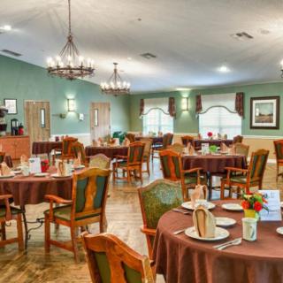 A cozy dining room with neatly arranged tables and chairs, illuminated by elegant chandeliers.