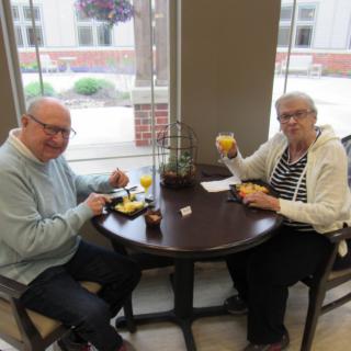 A senior couple enjoys a meal together at a small table by the window.