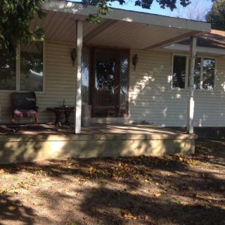 A sunny view of a house with a porch and steps, surrounded by trees.