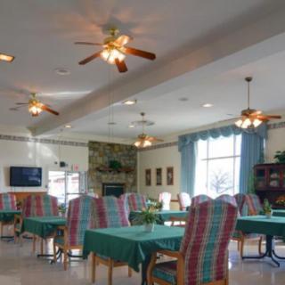 A cozy dining area with green tablecloths, ceiling fans, and ample natural light from a large window.