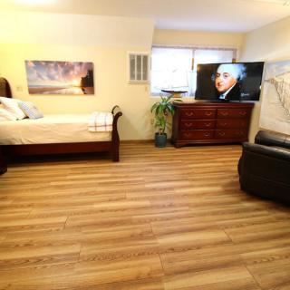 A cozy bedroom with wooden flooring, featuring a bed, dresser, television, and seating area.