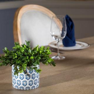 A dining table set with a decorative potted plant, wine glass, and folded napkin.
