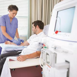 A nurse assists a patient undergoing dialysis treatment with medical equipment in a healthcare setting.