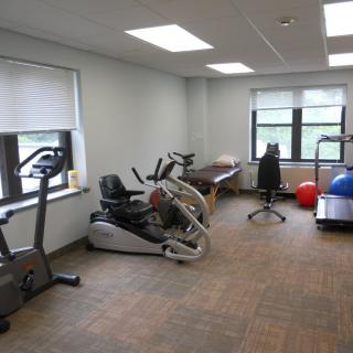 A small fitness room with various exercise equipment, including stationary bikes, therapy balls, and a treadmill.