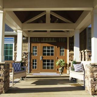 A welcoming front porch with stone columns and a wooden door, featuring outdoor seating.