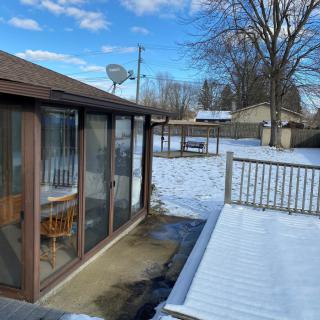 A snowy backyard with a sunroom and deck on a sunny winter day.