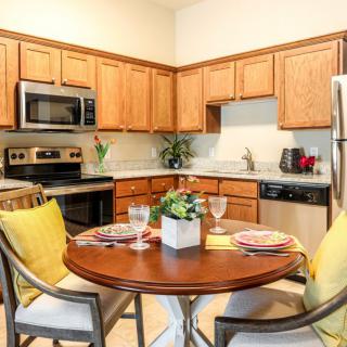 A modern kitchen and dining area with wooden cabinets, stainless steel appliances, and a round table set for dining.