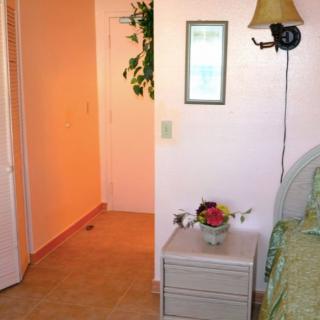 A cozy bedroom corner with a nightstand, lamp, and decorative plant by the doorway.