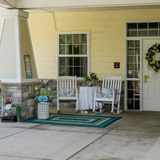 A cozy porch with rocking chairs, a wreath on the door, and decorative flowers.