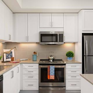 A modern kitchen with white cabinets and stainless steel appliances, featuring a microwave, oven, and refrigerator.
