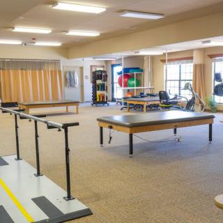 A spacious physical therapy room equipped with parallel bars and therapy tables.