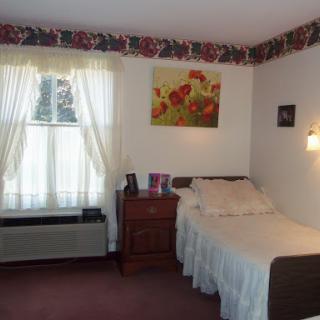 A cozy and well-decorated bedroom featuring a twin bed, floral wallpaper, and natural light from the window.