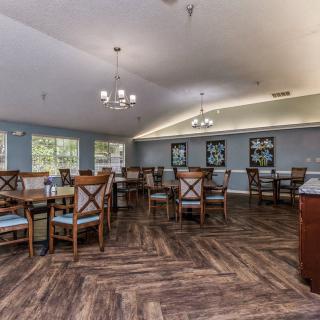 A spacious dining room with wooden flooring and neatly arranged tables and chairs.