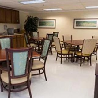 A clean and organized dining area with several tables and chairs, featuring a kitchenette in the background.