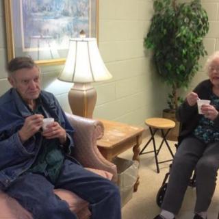 Two elderly individuals sitting indoors, enjoying drinks and relaxing.