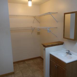 A small room featuring a sink, mirror, and shelving for storage.