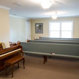 An interior room with a piano and several benches arranged in rows.