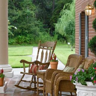 A cozy porch with wicker chairs and a rocking chair surrounded by lush greenery.