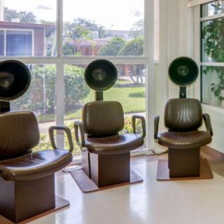 A modern hair salon featuring three stylish chairs with attached hair dryers in a bright, airy space.