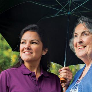 Two people smiling under an umbrella outdoors.
