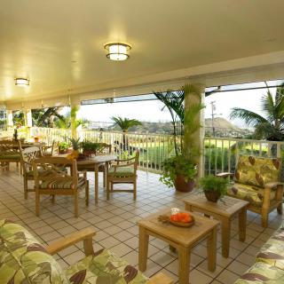 A cozy covered patio with tables and chairs, surrounded by tropical plants.