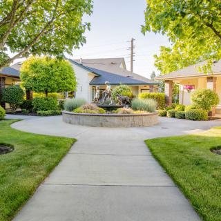 A tranquil garden with a circular pathway surrounded by lush greenery and trees, leading to charming houses.