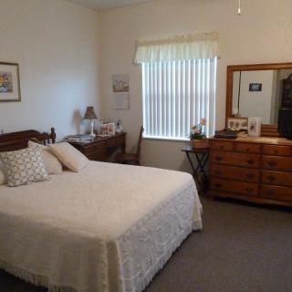 A cozy bedroom with a bed, dresser, and mirror beside a window.
