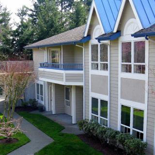 A stylish residential building featuring a blue roof and multiple balconies surrounded by lush greenery.