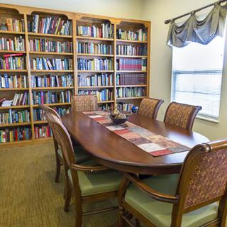 A cozy reading room with a large table surrounded by chairs and bookshelves filled with books.