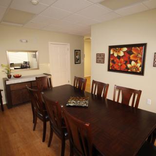 A well-furnished dining room with a long wooden table, surrounded by chairs and adorned with artwork on the wall.