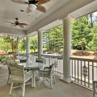 A spacious outdoor porch with wicker furniture and ceiling fans, offering a relaxing view of surrounding greenery.