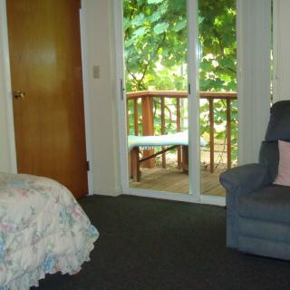 A cozy bedroom with a sliding door leading to a balcony, featuring a comfortable chair and a floral bedspread.