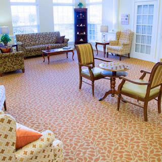 A well-lit living room with multiple chairs, a couch, and coffee tables on a patterned carpet.