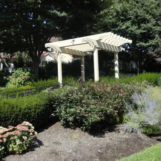A white pergola surrounded by lush greenery and neatly trimmed shrubs in a garden setting.