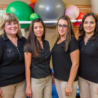 A group of four women standing together in a fitness environment, surrounded by colorful exercise equipment.