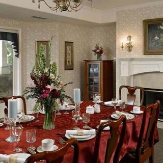 A formal dining room with an elegantly set table featuring a red tablecloth and floral centerpiece.
