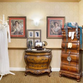A vintage-themed room featuring antique furniture, artwork, and a dress form.