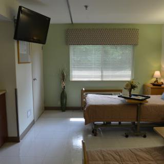 A peaceful hospital patient room featuring two beds, a TV, and natural light coming through the window.