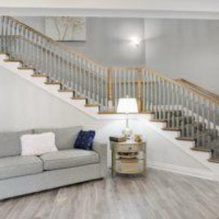 A modern living room featuring a stylish staircase, a comfortable gray sofa, and a cozy lamp on a side table.