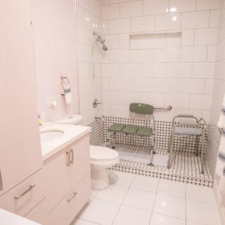 An accessible bathroom with a walk-in shower, safety chairs, and white tiled walls.