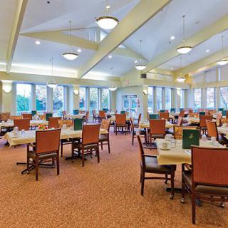 A spacious dining room with neatly arranged tables and chairs, featuring large windows and a carpeted floor.