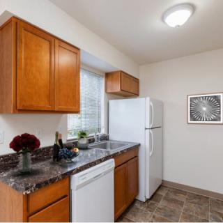 A modern kitchen featuring wood cabinets, a granite countertop, and standard appliances such as a refrigerator and dishwasher.