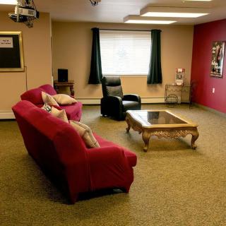 A cozy living room with a red sofa, recliner chair, and a glass coffee table on a carpeted floor.