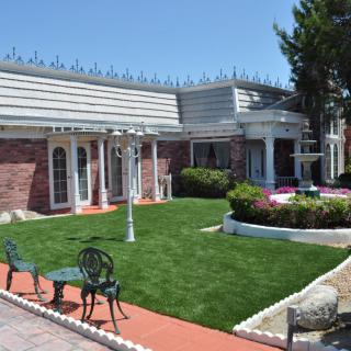 A well-maintained yard with green grass, benches, and a brick house in the background.
