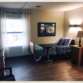 A well-lit patient room featuring a hospital bed, bedside lamp, and a window with sheer curtains.