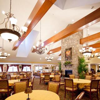 A spacious dining room with elegant chandeliers, wooden beams, and a stone fireplace.