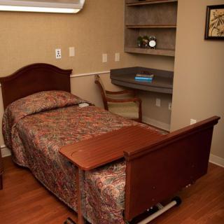 A bedroom with a hospital-style bed, a small desk, and wooden furnishings.