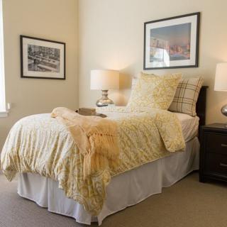 A cozy bedroom with a neatly made bed, two side lamps, and framed artwork on the walls.
